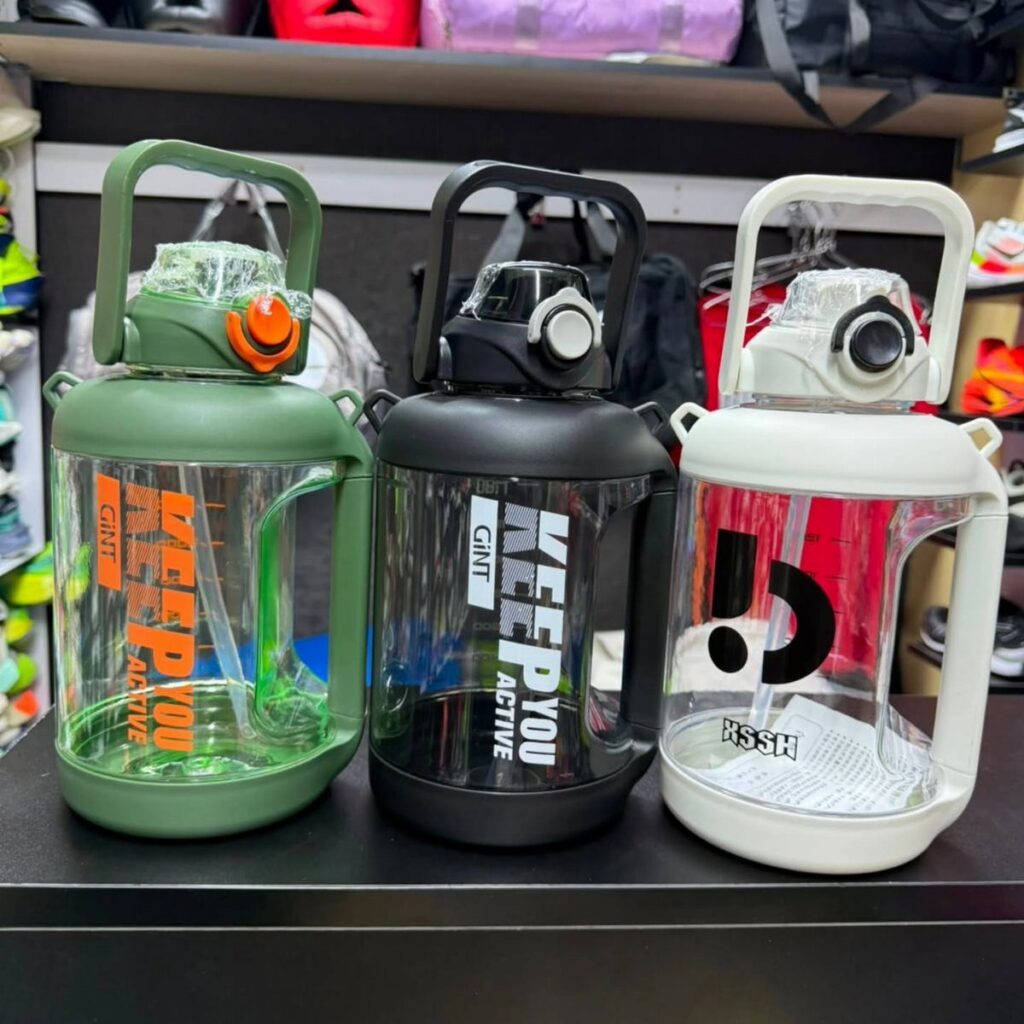 Three large plastic water jugs in green, black, and white on a shelf.