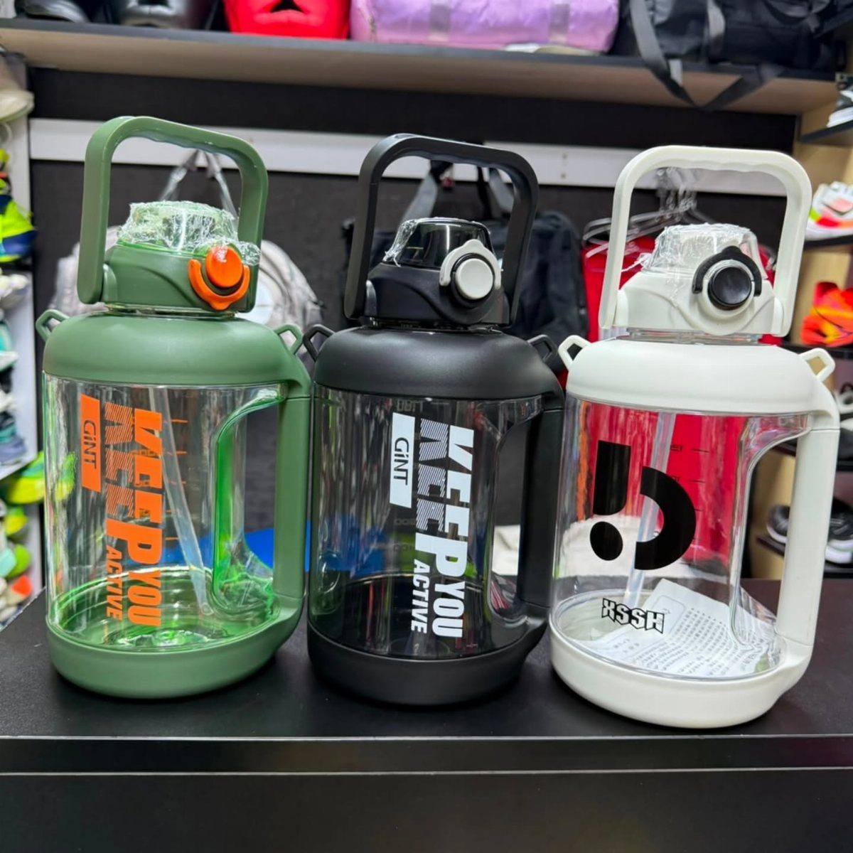 Three large plastic water jugs in green, black, and white on a shelf.
