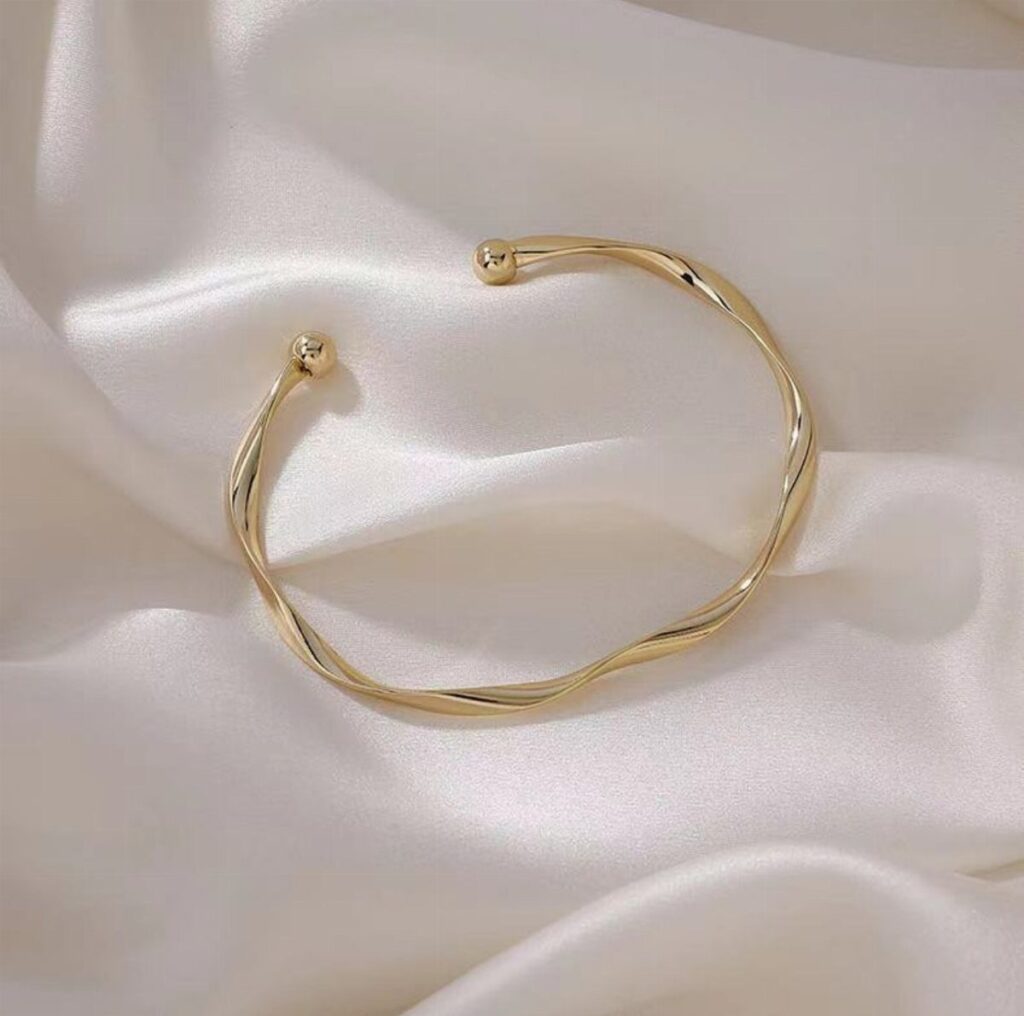 Gold twisted-cuff bracelet resting on draped white satin fabric