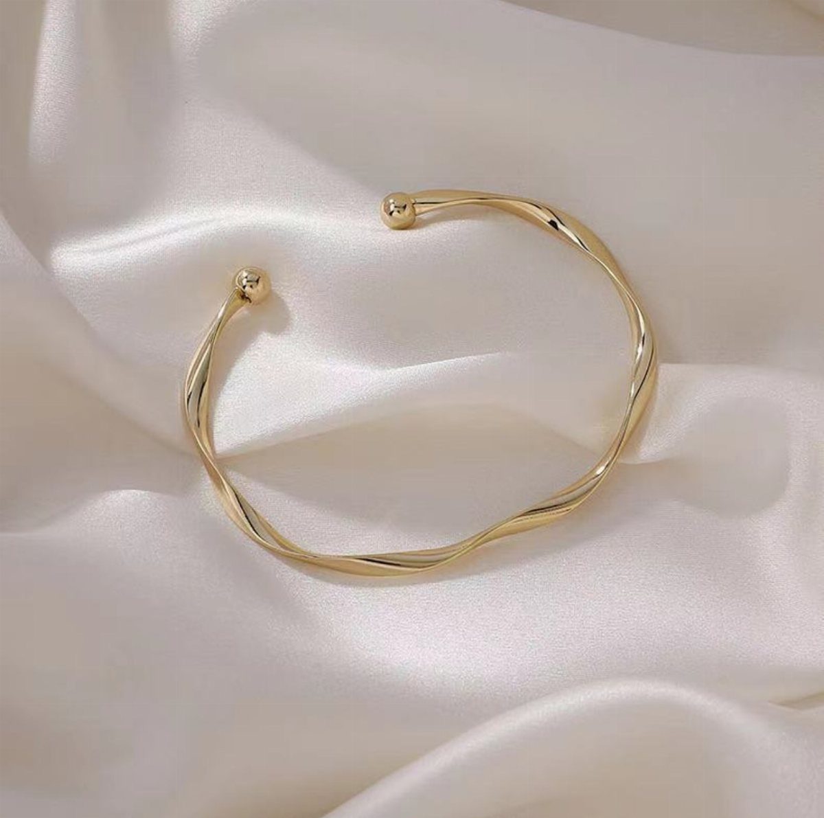 Gold twisted-cuff bracelet resting on draped white satin fabric