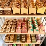 Artisanal handmade soaps in festive shapes and colors displayed on white shelves.