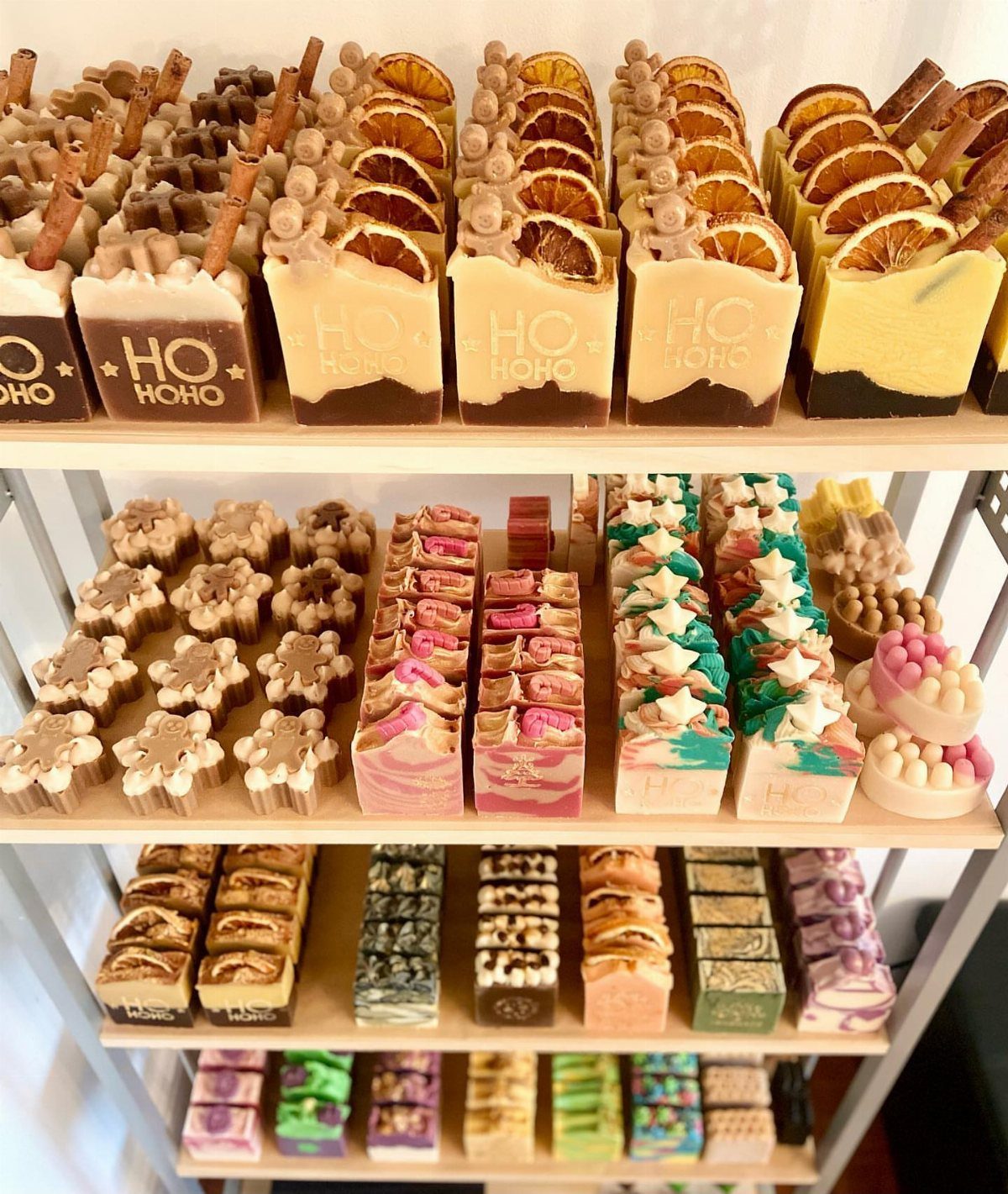 Artisanal handmade soaps in festive shapes and colors displayed on white shelves.