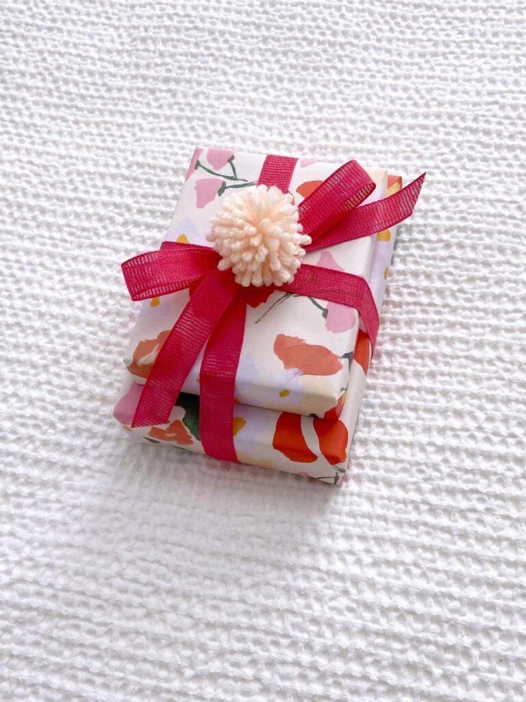 Floral wrapped gifts with red ribbons and a white pom pom topper.