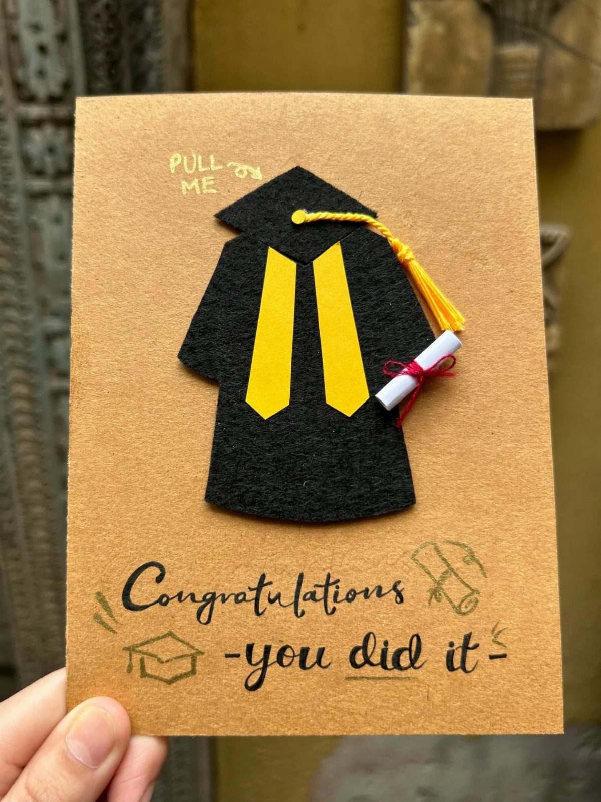 Handmade graduation card with a felt gown, diploma, and congratulations message.