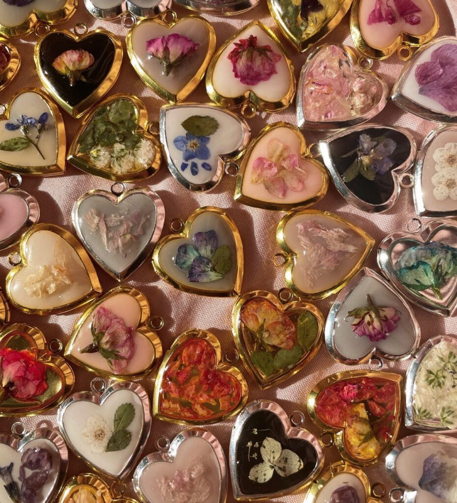 Heart-shaped resin pendants containing pressed dried flowers on a pink fabric background.