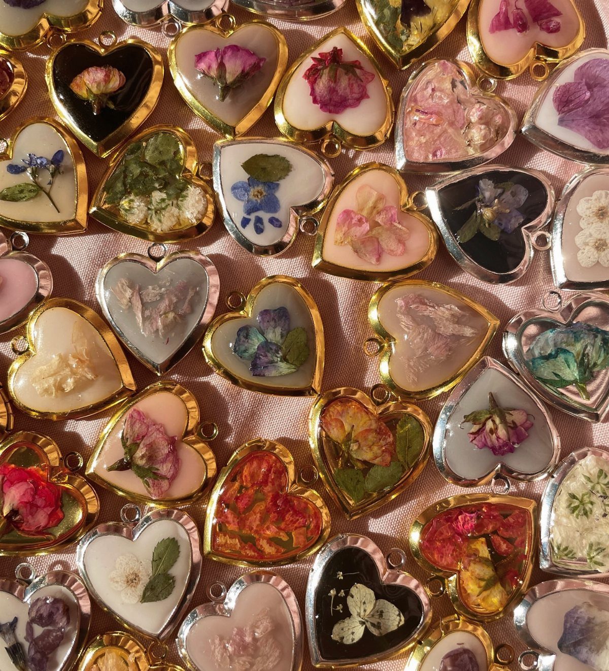 Heart-shaped resin pendants containing pressed dried flowers on a pink fabric background.