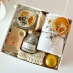 Spa gift box with bath salt, gold bath bomb, candle, and white towel.