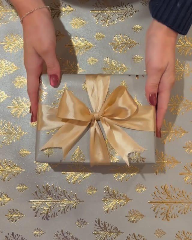 Hands holding a silver gift box with a large gold satin bow
