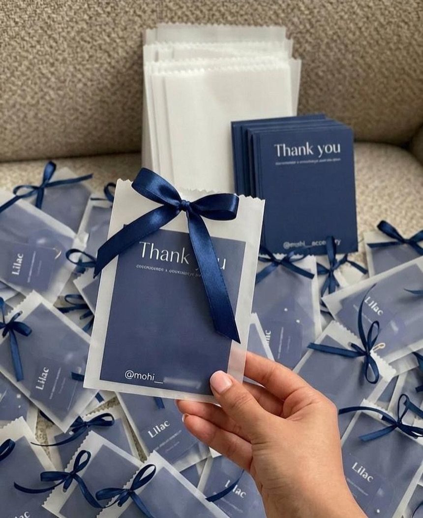 Small translucent white organza gift bags tied with navy blue ribbons containing thank you cards.