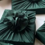 Dark green satin wrapped gifts featuring large ruffled fabric flower ornaments on top