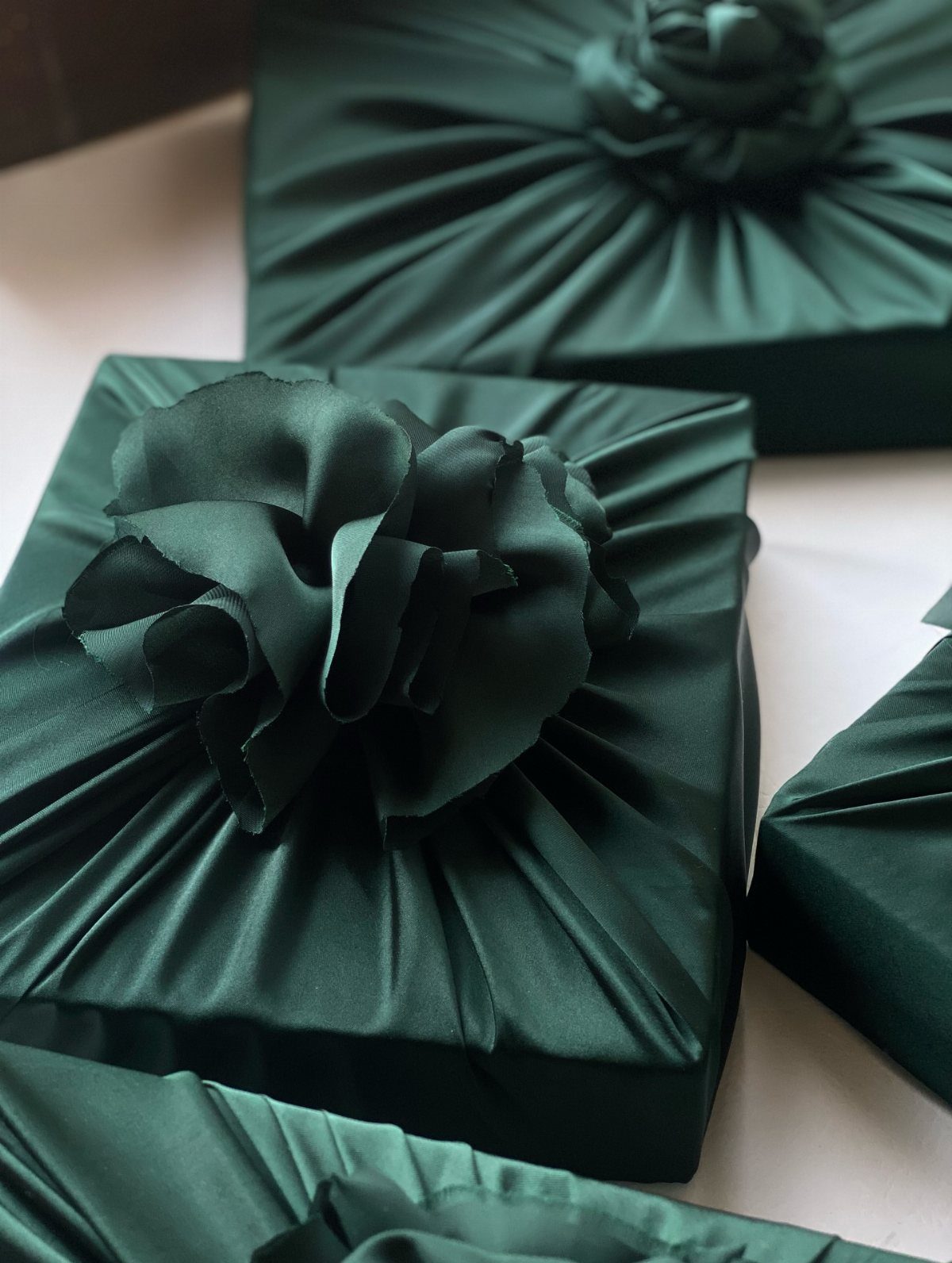 Dark green satin wrapped gifts featuring large ruffled fabric flower ornaments on top