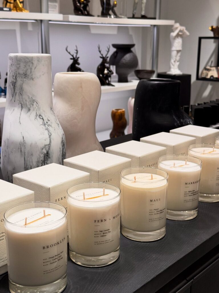 White scented candles in glass jars lined up on a dark display shelf