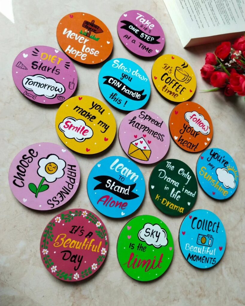 Colorful circular handmade magnets with motivational quotes and drawings on a light surface.