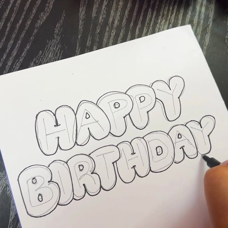 Hand drawing bubble letters saying Happy Birthday on a white paper card.