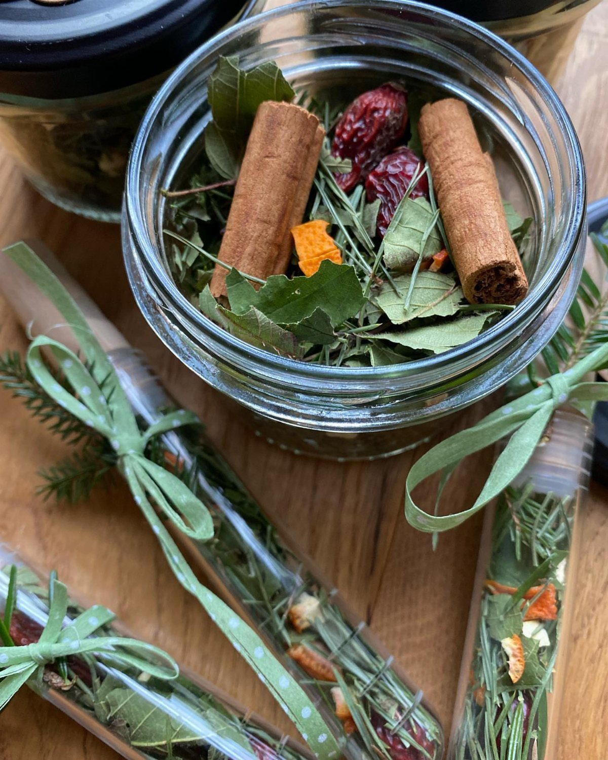 Dried cinnamon sticks and botanicals in a glass jar and ribbon-tied tubes.