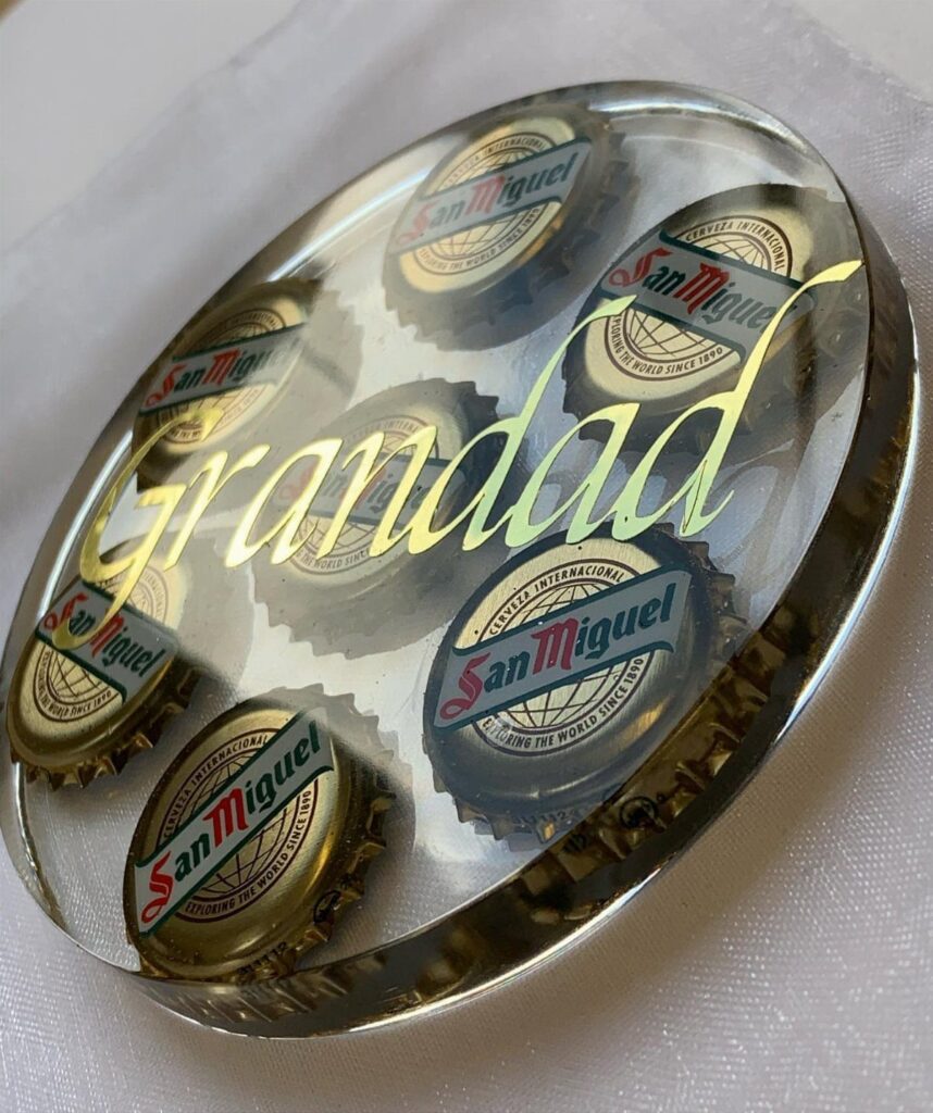 Oval resin coaster with beer bottle caps and gold Grandad script on white fabric