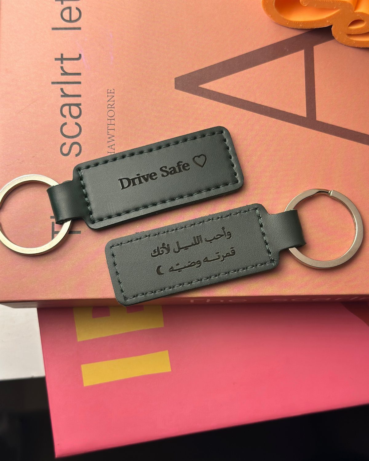 Two dark grey leather keychains with engraved messages resting on a pink book.