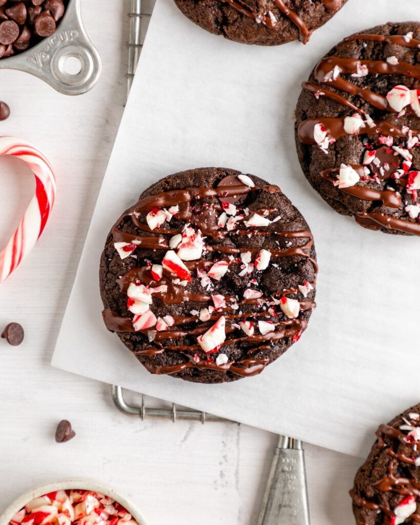 Chocolate peppermint cookies with ganache drizzle and crushed candy on parchment paper