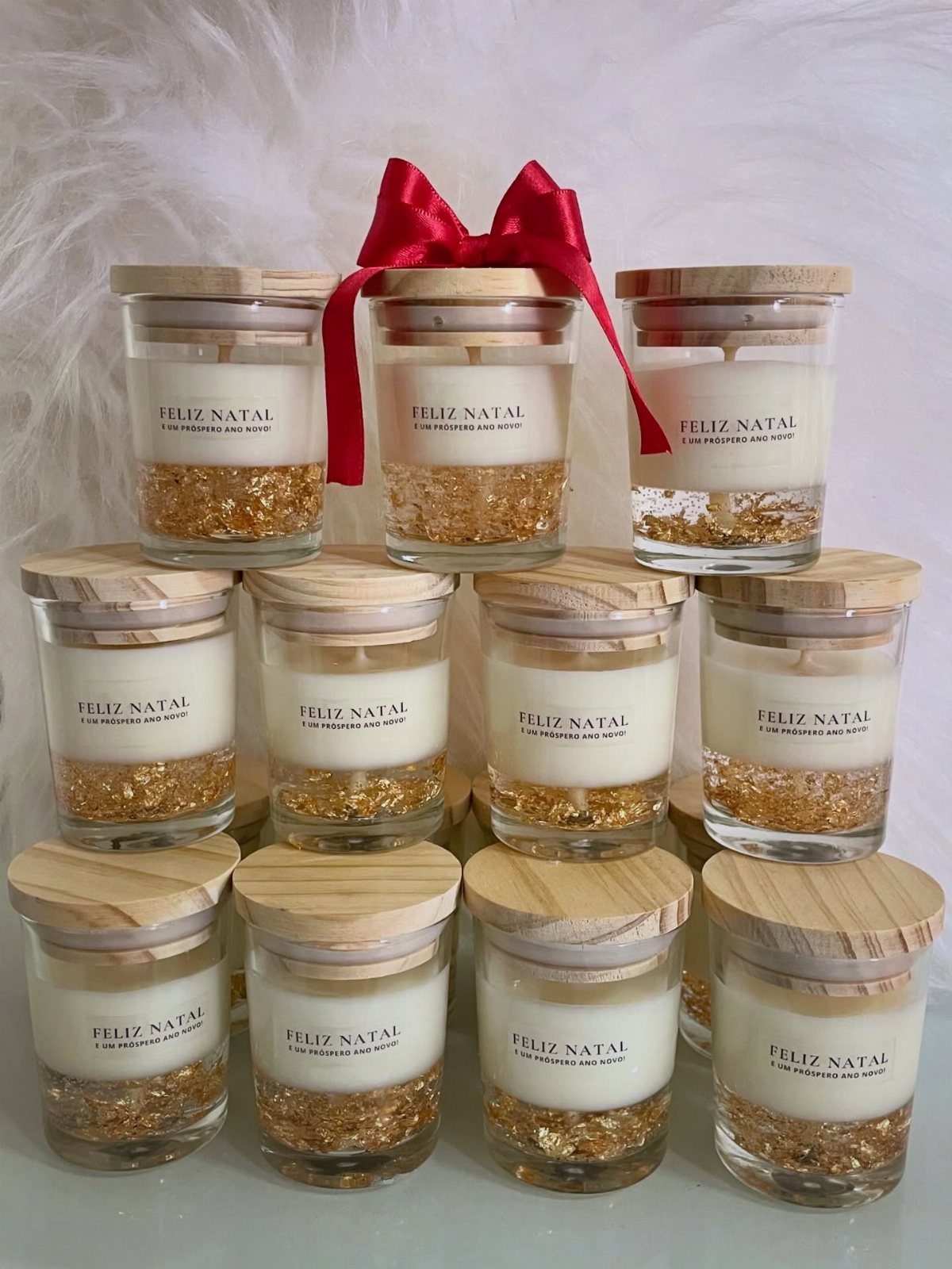 Twelve white scented candles in glass jars with wooden lids and red ribbon.