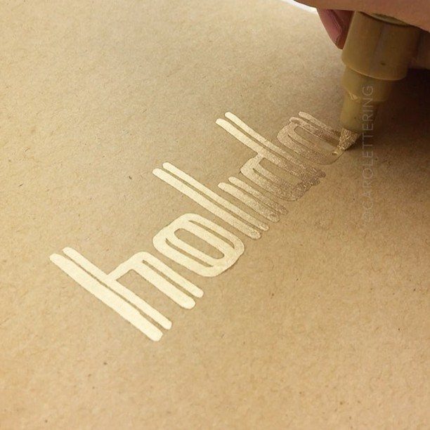 Gold paint marker writing the word holiday on brown kraft paper
