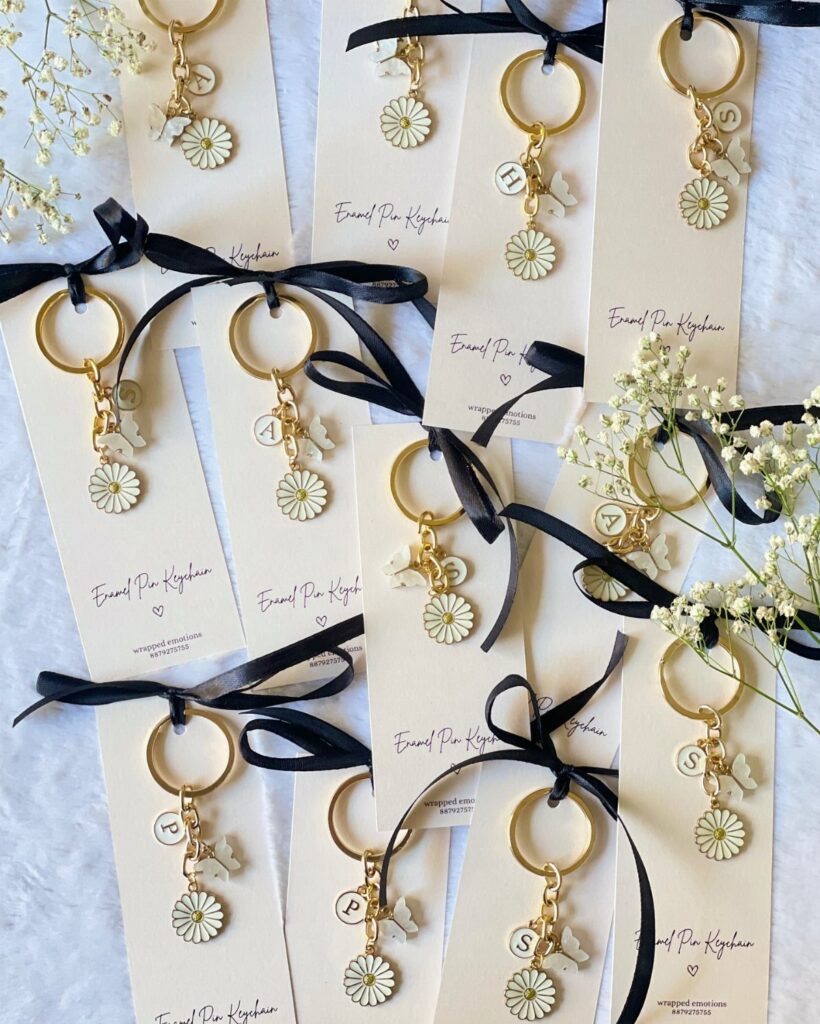 Gold keychains with daisy charms and letter beads on white cards with ribbons.