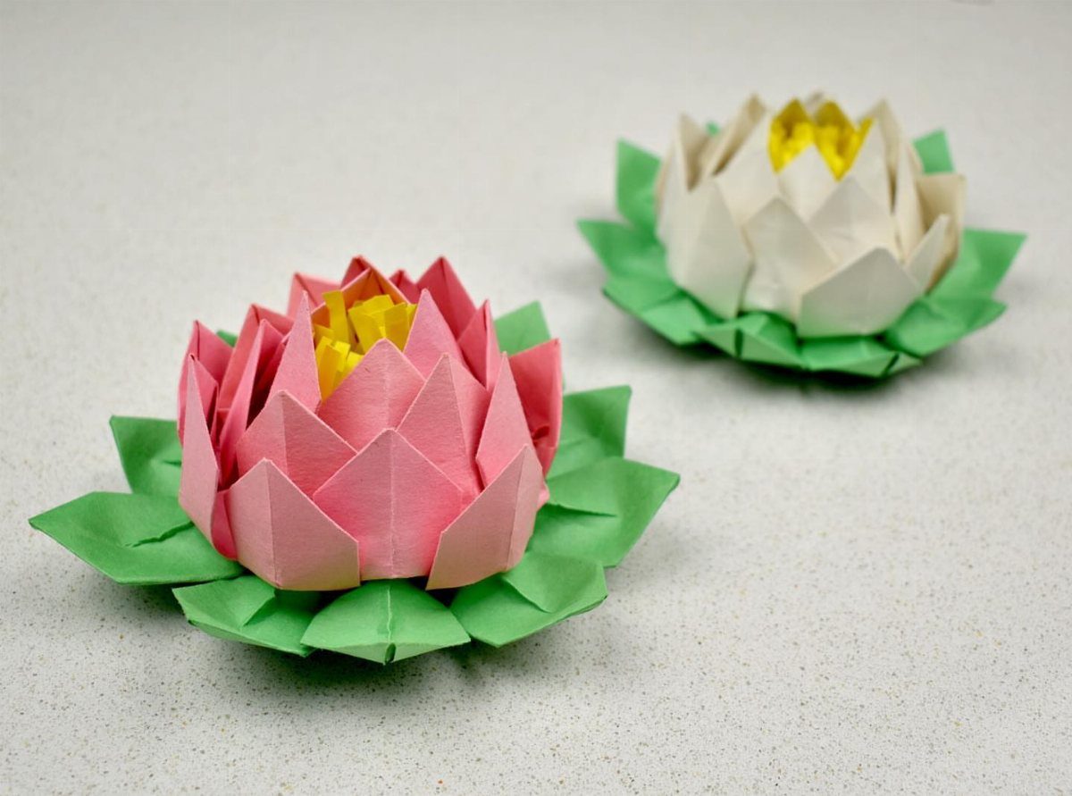 Two folded paper lotus flowers in pink and white with green leaves.