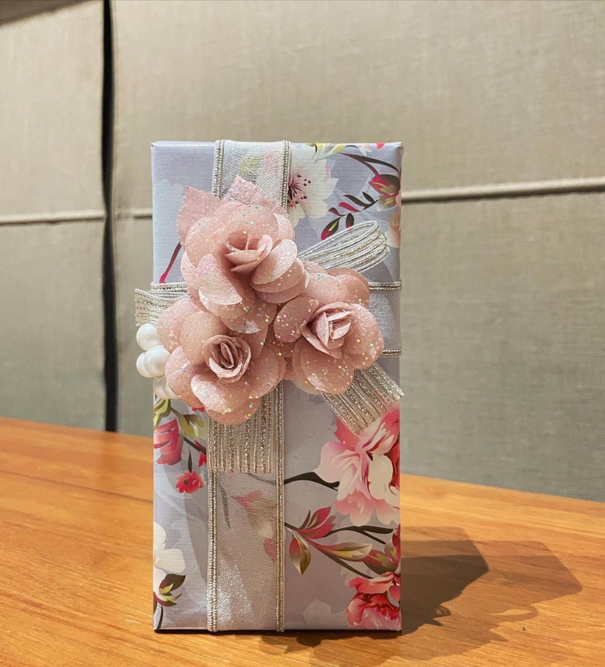 Floral wrapped gift with silver glitter ribbon and pink fabric roses on wood.