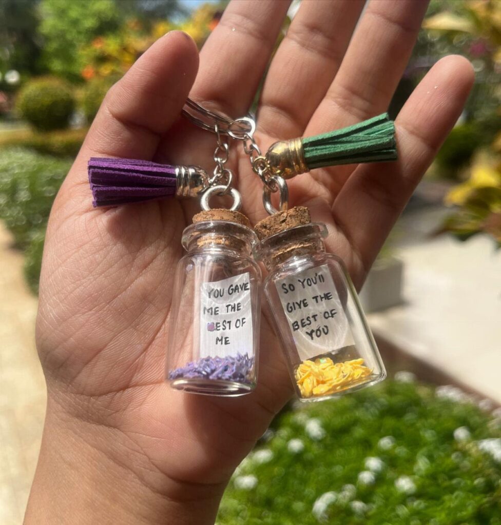Two small glass bottle keychains with notes and tassels held in a hand.