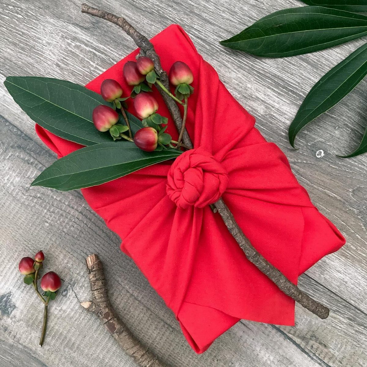 Red fabric wrapped gift with a knot, decorated with berries and a twig.